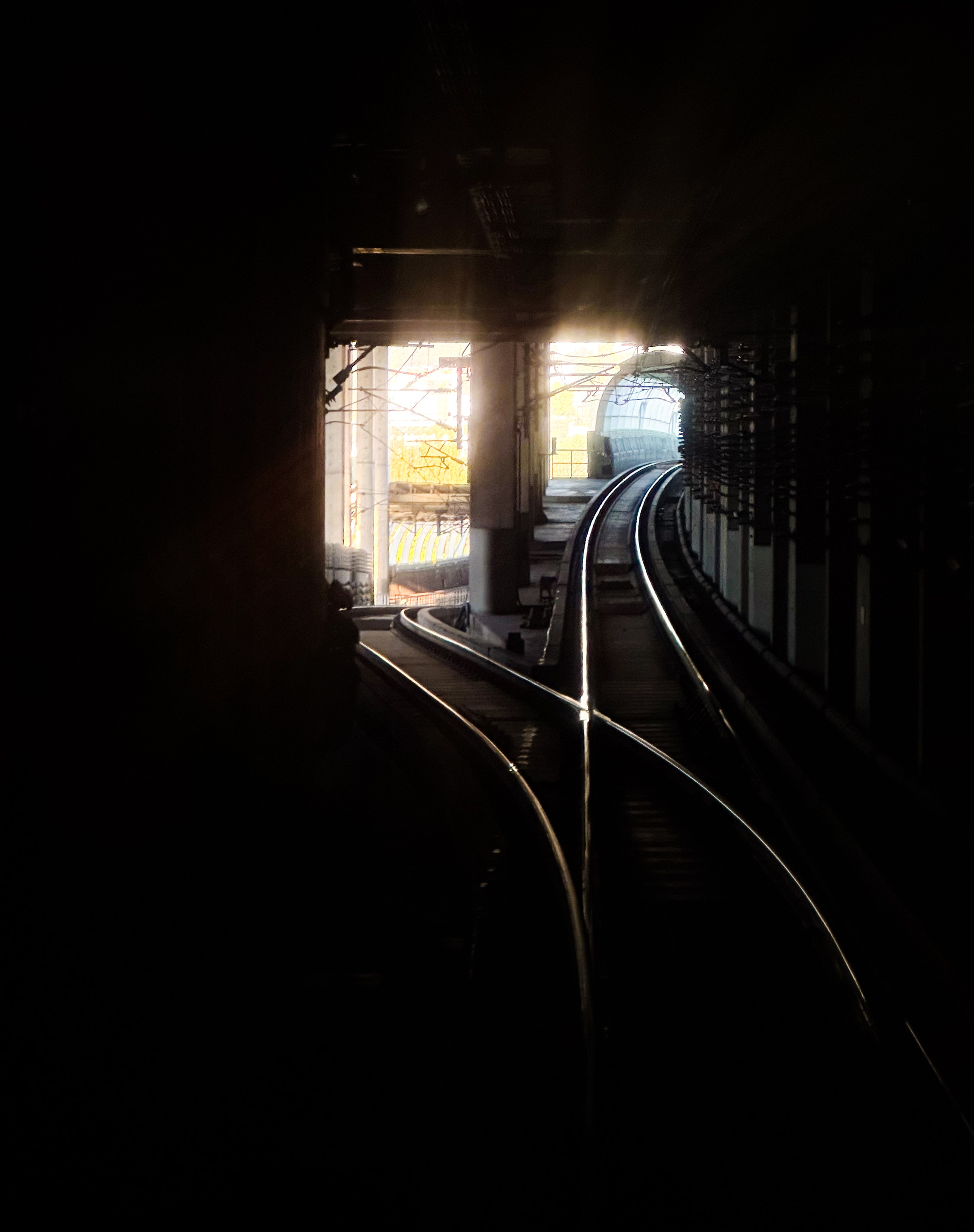 Blick aus einem dunklen Tunnel an einer Weiche. Man sieht wie die sich trennende Strecke an zwei verschiedenen Tunnelenden ins Helle führt.