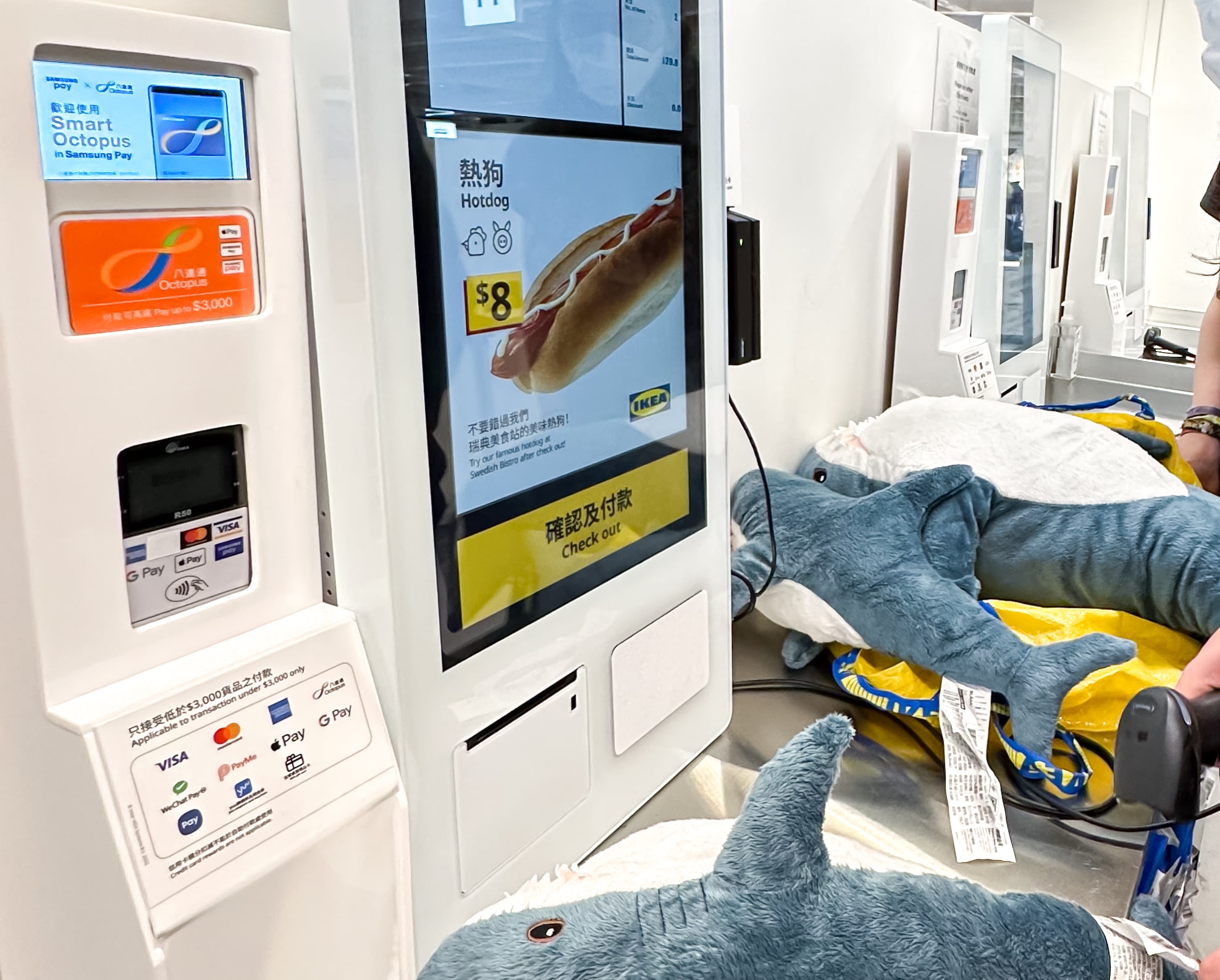 Eine Self-Checkout Kasse auf der gerade IKEA Blåhaj gescannt werden. Die Kasse hat einen reader für Octopus Karten.