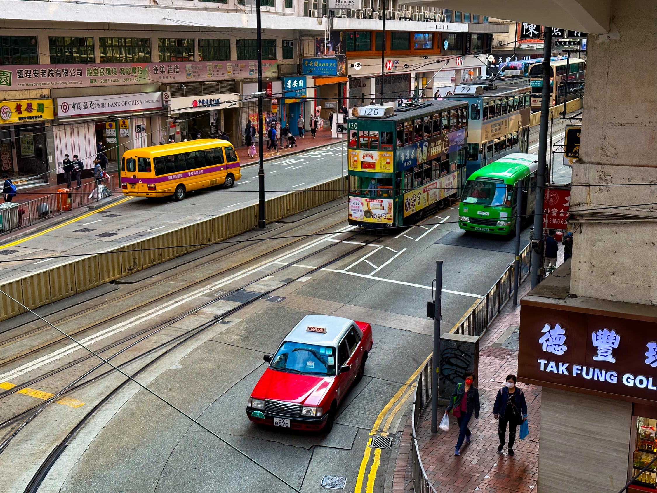Eine Kreuzung mit Weiche von oben. Zwei Trams, ein Taxi und zwei kleiner Busse sind auf der Straße zu sehen.