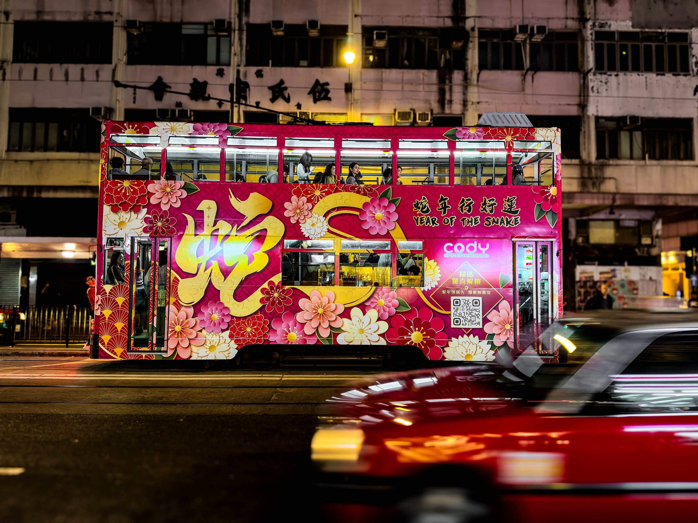 Eine Tram mit Pinker Werbung leuchtet durch die Nacht. Davor fährt ein Taxi.