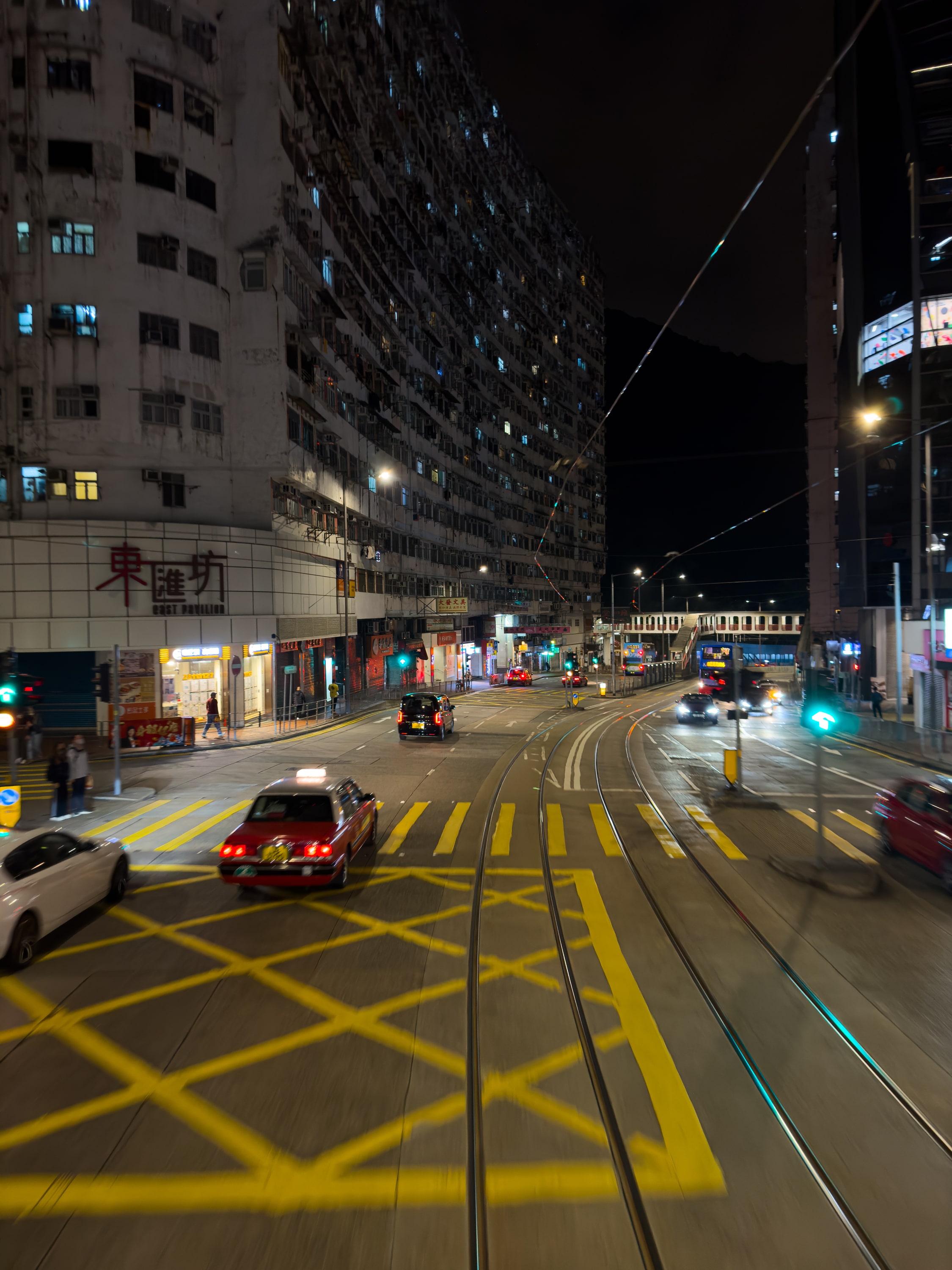 Eine Nächtliche Straße. Etwas Bewegungsunschärfe entlang des Fahrtwegs der Straßenbahn. Ein Taxi überholt.