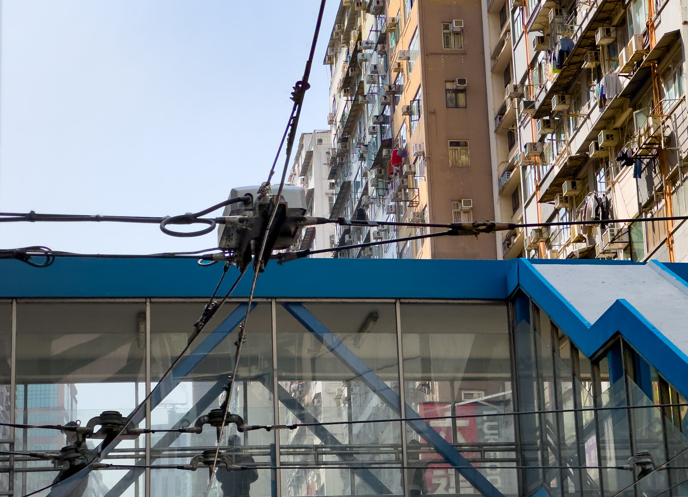 Blick von unten auf die Oberleitung. Über dieser hängt ein Kasten. Ein kleines Stück Oberleitung unter dem Kasten ist felxibel und kann in beide Seiten des Fahrtweges bewegt werden.