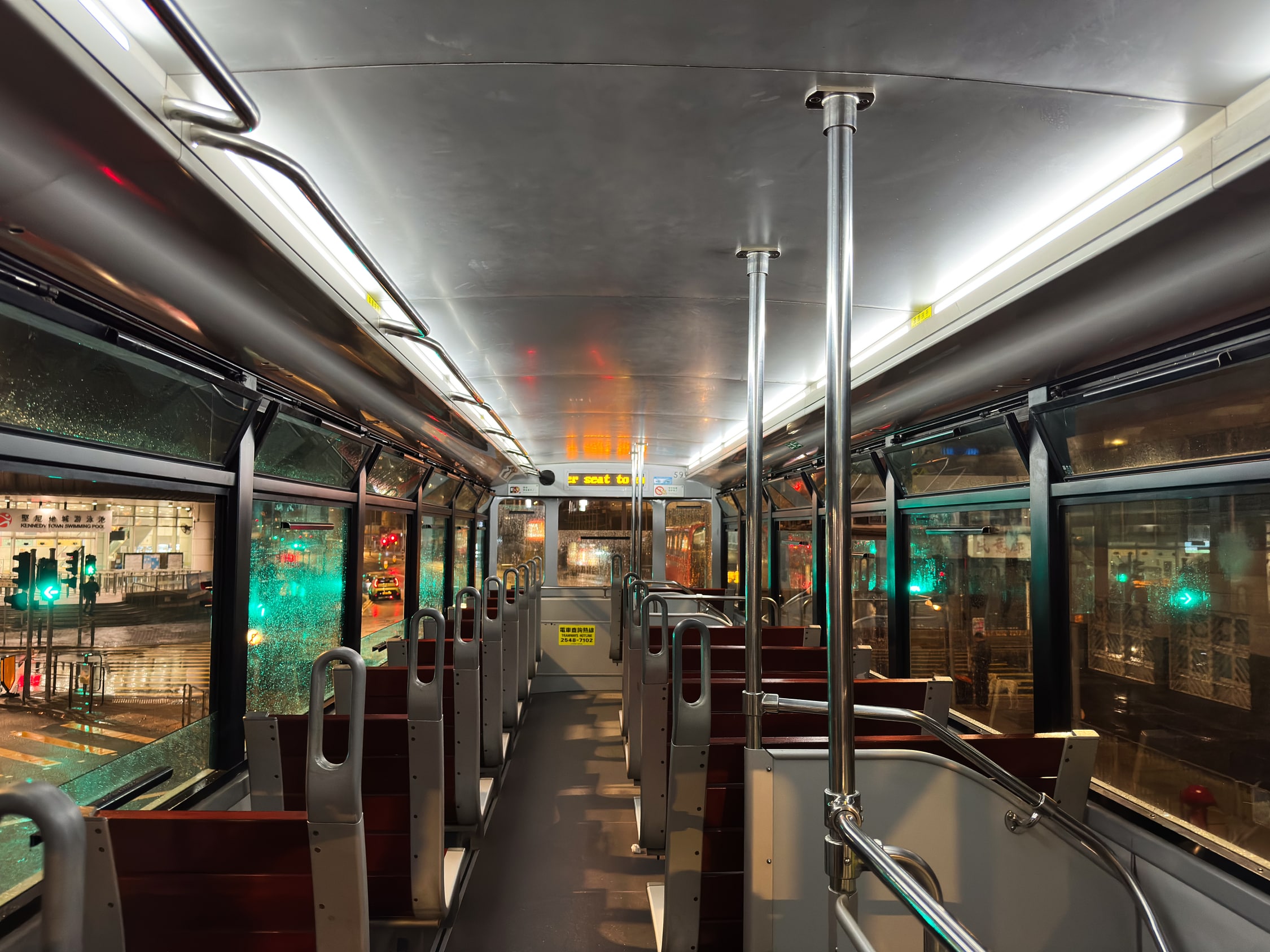 Oberes Deck der Straßenbahn von innen. Einige Fenster sind offen. An den geschlossenen Fenstern sieht man, dass die außen voll mit Regentropfen sind und sich das Licht einer Ampel darin stark reflektiert.