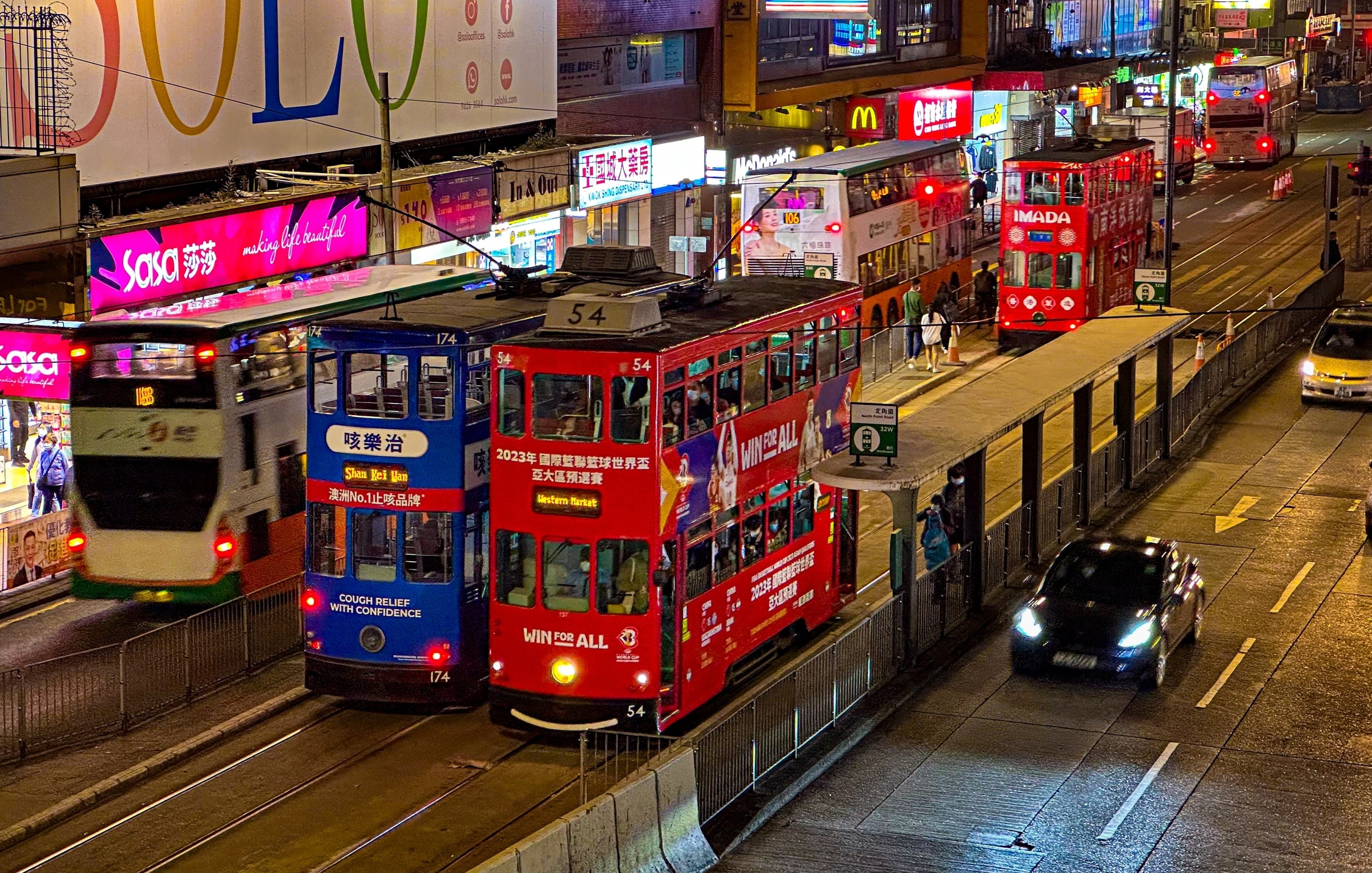 Eine nächtliche Straßenszene in der mehrere Doppelstocktrams zu sehen sind