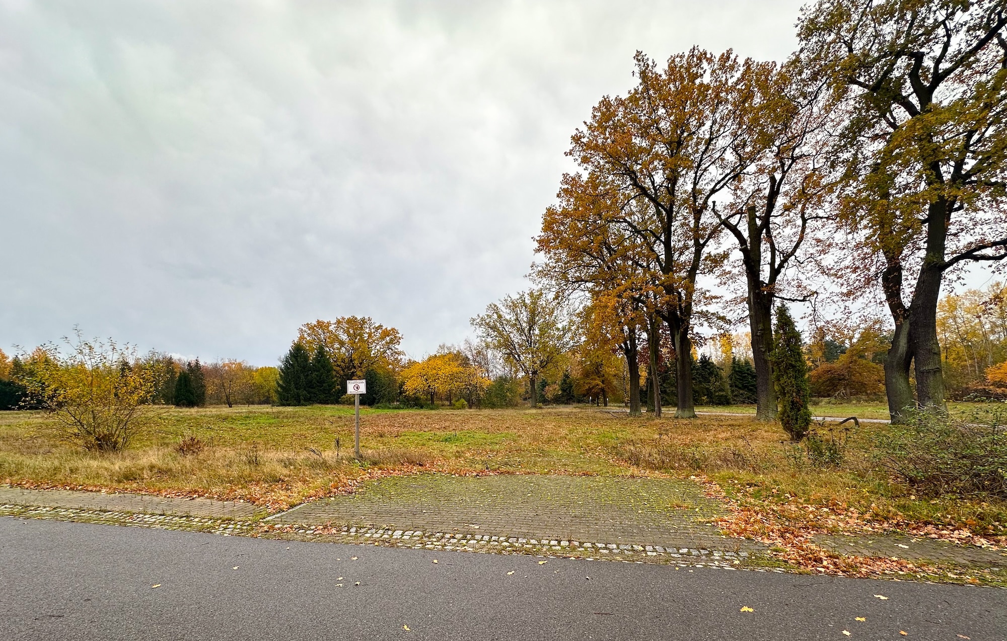 Ein schild steht am Straßenrand, direkt neben einer Stelle die anders gepflastert ist, son dass eine Einfahrt zu einem Hof erahnbar ist.