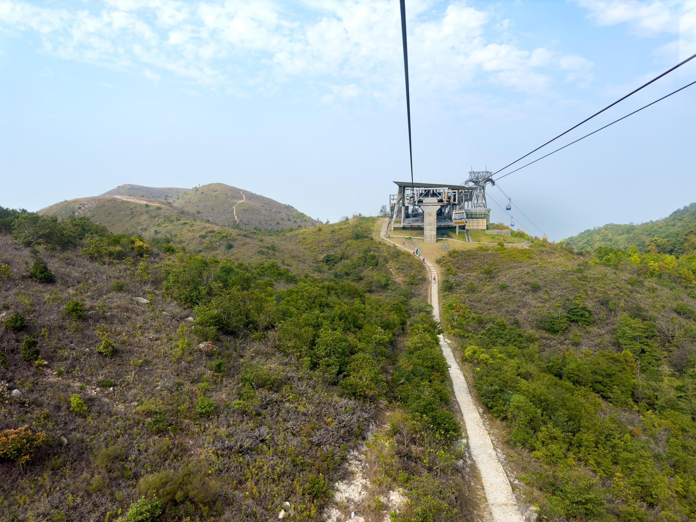 Eine Seilbahn Winkelstation auf einer Bererhöhung. Unter den Seilen führt ein Weg bis zur Station und an dieser Vorbei. Im Hintergrund nur mit Gras und Gestrüpp bewachsene Berge.